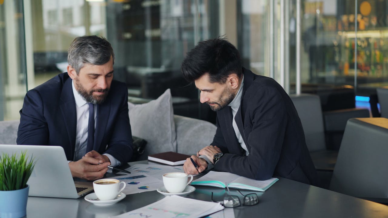 Two people wearing suits sitting at a table looking at charts